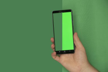 A man's hand on a green background holds a mobile phone with a green screen, a template with a phone, a green screen, a photo before and after cutting the background, an example