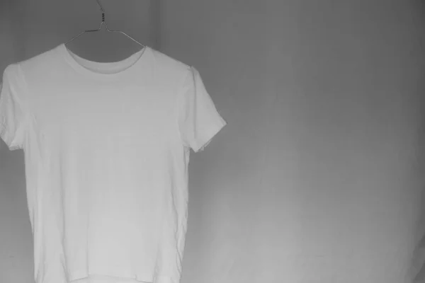 White T-shirt hanging on a hanger in the dark, black and white photo, fashionable clothes