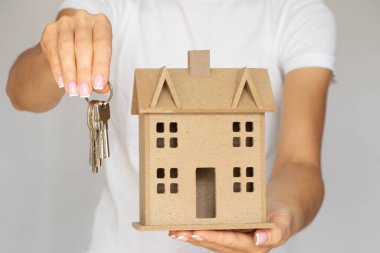 House keys and a small wooden decorative house in the hands of a girl on a white background, rent and purchase of real estate, house and apartment
