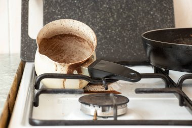 Dirty Turk from coffee lies on a gas stove in the kitchen with spilled coffee, morning coffee, dirty tiles