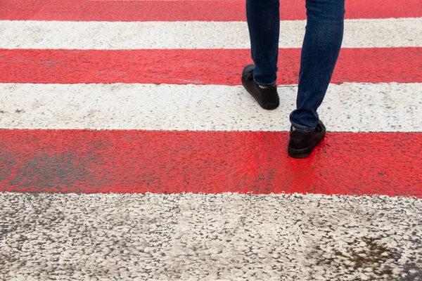 A man crosses the road at a pedestrian crossing, feet on the road, go to the front