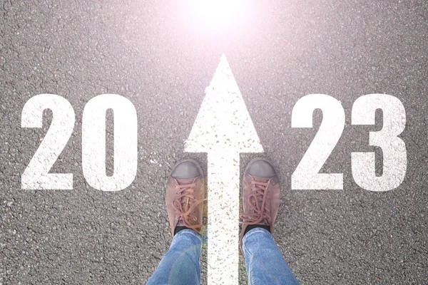 Women\'s feet stand on the forward arrows on the road and text on the road 2023, happy new year 2023, start of a new year, start and success in the new year
