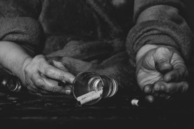 Sigara bir bardak ve boş bir şişe ve yanmış siyah bir masanın üzerinde yaşlı bir kadının elleri, sigara ve alkolizm, kötü alışkanlıklar.