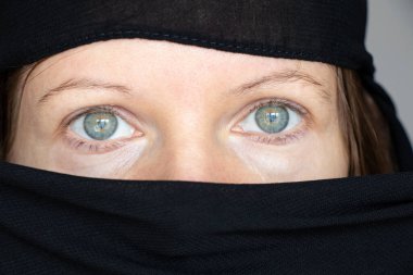 Kız yüzünü ve başını siyah bir eşarpla örtmüş, izole bir arka planda, inanç ve din Müslümandır.