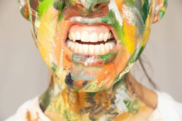 A girl with a face painted with paints with her mouth wide open, teeth and mouth, screaming