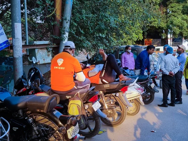 Swiggy παράδοση τροφίμων αναβάτη κάθεται σε ποδήλατο περιμένοντας για την παραγγελία takeaway σε πορτοκαλί πουκάμισο, ενώ οι άνθρωποι περιφέρονται γύρω — Φωτογραφία Αρχείου