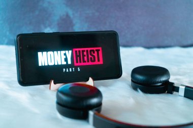 Mobil akıllı telefon kürklü kar yüzeyine yerleştirilmiş kulaklıklarla ayakta Para Soygunu 'nun popüler netflix şovunu seyrediyor.