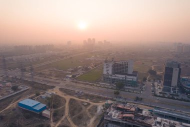 Hava aracı, evleri, ofisleri, alışveriş merkezleri olan bir binanın üzerinden geçerken gün batımının önündeki gökdelenlere doğru ilerlerken, Gurgaon şehrinin boş mahallelerini gösteriyor.