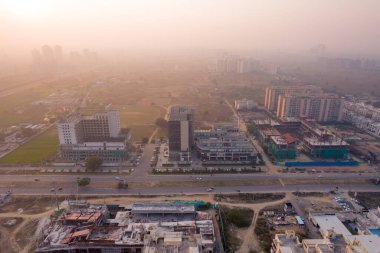 Hava aracı, evleri, ofisleri, alışveriş merkezleri olan bir binanın üzerinden geçerken gün batımının önündeki gökdelenlere doğru ilerlerken, Gurgaon şehrinin boş mahallelerini gösteriyor.