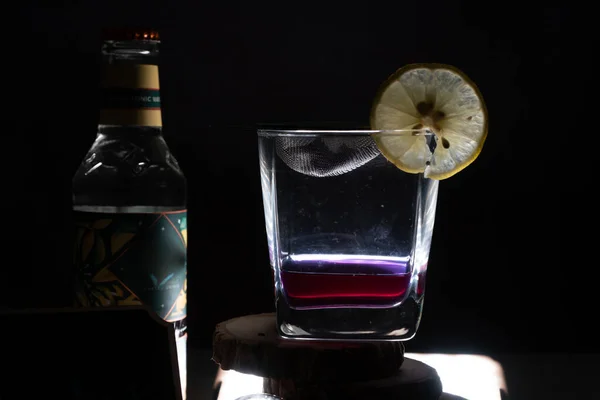 Plano de luz sobre fondo negro que muestra fileld de vidrio con ginebra de vino infundido con especias con cuña de limón y botella de tónico en el lateral para una bebida de celebración —  Fotos de Stock