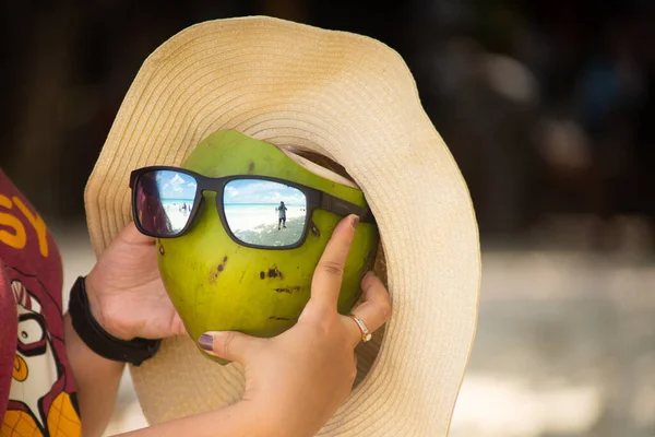 Zbliżenie strzał kobieta gospodarstwa kokos noszenie kapelusz i okulary przeciwsłoneczne pokazujące nastrój wakacje na tropikalnej plaży w lecie — Zdjęcie stockowe