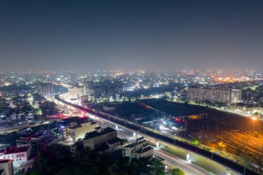 Şehir ışıklarıyla çevrili binalar ve metro istasyonları ile çevrili ışıklı bir yol üzerinden geçen yüksek metro yolu.