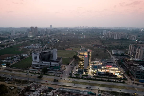 Toma aérea del atardecer que muestra el centro comercial de 3 carreteras iluminado con los edificios en construcción a su alrededor sin iluminación mientras el sol se pone — Foto de Stock