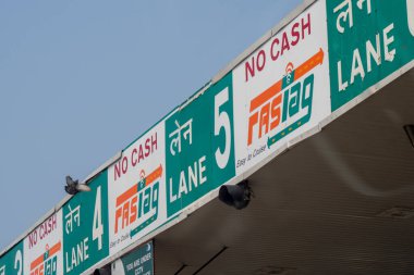 Yeni RFID tabanlı ödeme sistemini gösteren bir gişenin önünde sıkışık trafik sıkışıklığı arabaları ve Hindistan Ulusal Otoyol İdaresi NHAI logosu.