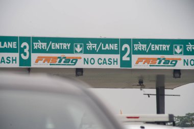Yeni RFID tabanlı ödeme sistemini gösteren bir gişenin önünde sıkışık trafik sıkışıklığı arabaları ve Hindistan Ulusal Otoyol İdaresi NHAI logosu.