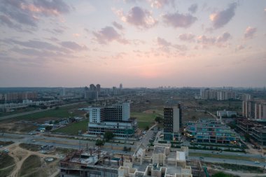 Hava alacakaranlık görüntüleri, Gurgaon 'daki 3 yol alışveriş merkezini gösteriyor. Işıklar açık ve trafik ön taraftaki yoğun yolda ve inşaat alanlarında ilerliyor.