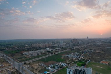 Hava aracı, evleri, ofisleri, alışveriş merkezleri olan bir binanın üzerinden geçerken gün batımının önündeki gökdelenlere doğru ilerlerken, Gurgaon şehrinin boş mahallelerini gösteriyor.
