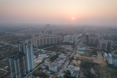Hava aracı, evleri, ofisleri, alışveriş merkezleri olan bir binanın üzerinden geçerken gün batımının önündeki gökdelenlere doğru ilerlerken, Gurgaon şehrinin boş mahallelerini gösteriyor.