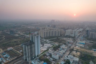 Hava aracı, evleri, ofisleri, alışveriş merkezleri olan bir binanın üzerinden geçerken gün batımının önündeki gökdelenlere doğru ilerlerken, Gurgaon şehrinin boş mahallelerini gösteriyor.