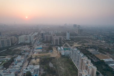 Hava aracı, evleri, ofisleri, alışveriş merkezleri olan bir binanın üzerinden geçerken gün batımının önündeki gökdelenlere doğru ilerlerken, Gurgaon şehrinin boş mahallelerini gösteriyor.