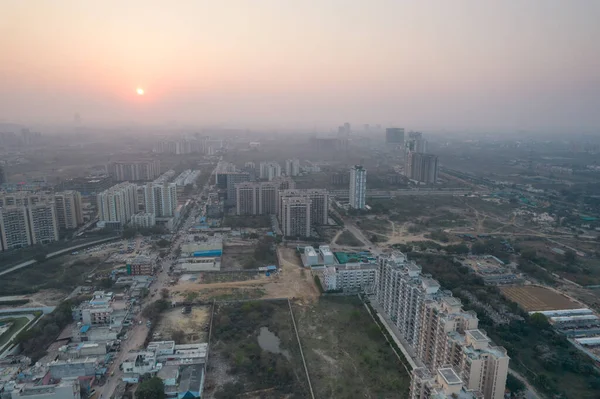 Aerial drone shot passing over a building with homes, offices, shopping centers moving towards skyscapers in front of sunset showing the empty outskirts of the city of gurgaon — 图库照片