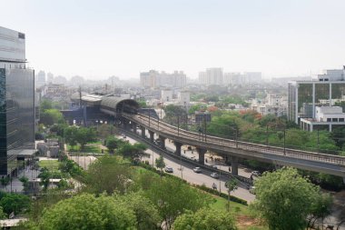 Camla kaplı gökdelenler, ağaçlı evler ve yüksek metro köprüsü, Gurgaon Delhi Hindistan 'daki toplu taşımayı gösteriyor.