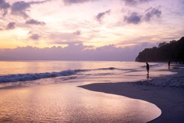 Siluet plajdaki bulanık insanları bulanıklaştırdı. Güzel turuncu, mavi bulutlu günbatımı Kalapathar plajında.