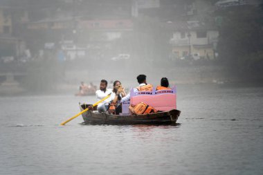 Nanital, Uttarakhand, India - circa 2022 : colorful shot of row boat with yellow paddles carrying red life jackets sitting and enjoying the beautiful ride in the foggy lake at bhimtal hill station
