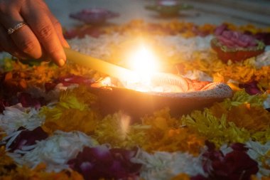 soft filter shot of person lighting diya oil lamp with a lit candle set in a rangoli bed of flowers showing the beautiful decorations on hindu festival of diwali India