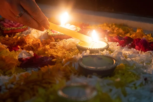 soft filter shot of person lighting diya oil lamp with a lit candle set in a rangoli bed of flowers showing the beautiful decorations on hindu festival of diwali India