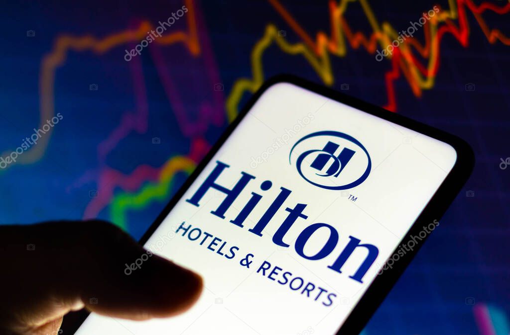 December 8, 2021, Brazil. In this photo illustration the Hilton Hotels and Resorts logo seen displayed on a smartphone and in the background a stock market graph