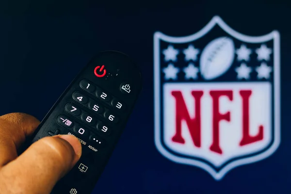 stock image February 21, 2022, Brazil. In this photo illustration a close-up of a hand holding a TV remote control seen displayed in front of the NFL Network logo