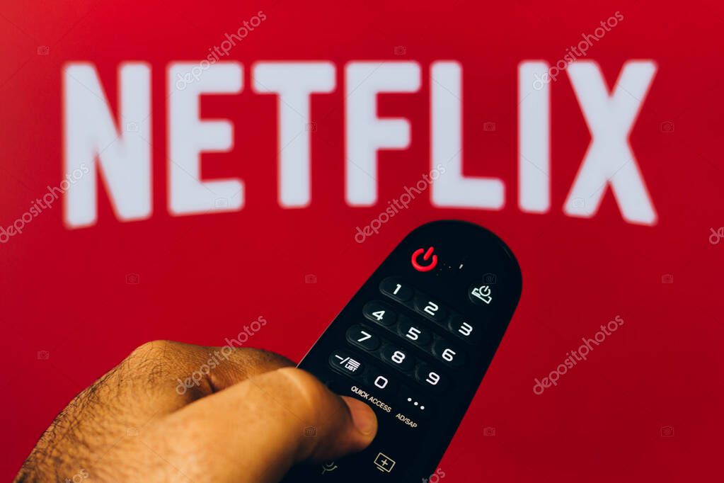 February 21, 2022, Brazil. In this photo illustration a close-up of a hand holding a TV remote control seen displayed in front of the Netflix logo