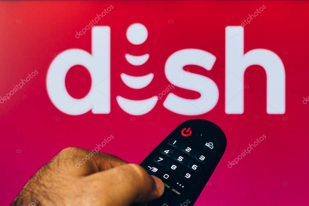 February 21, 2022, Brazil. In this photo illustration a close-up of a hand holding a TV remote control seen displayed in front of the Dish Network Corporation logo