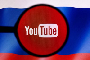 2 Mart 2022, Brezilya. Bu resimde, bir YouTube logosu bir büyüteçle ve arka planda Rusya bayrağıyla bilgisayar ekranında gösteriliyor.