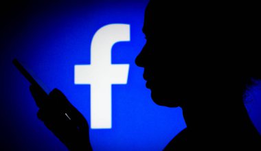 14 Mart 2022, Brezilya. Bu resimde Facebook logosu, elinde cep telefonu olan siluet bir kadının arka planında görülüyor.
