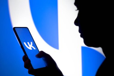 23 Mart 2022, Brezilya. Bu resimde, bir kadının silueti ekranda ve arka planda VKontakte (VK) logosunun gösterildiği bir akıllı telefon tutar.