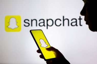 28 Mart 2022, Brezilya. Bu resimde, bir kadının silueti ekranda ve arka planda Snapchat logosu olan bir akıllı telefon tutuyor.