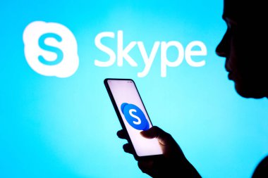 28 Mart 2022, Brezilya. Bu resimde, bir kadının silueti ekranda ve arka planda Skype logosu olan bir akıllı telefon tutuyor.