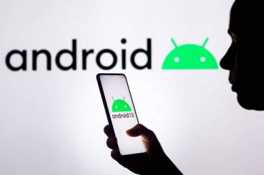 28 Mart 2022, Brezilya. Bu resimde, bir kadının silueti ekranda ve arka planda Android logosu olan bir akıllı telefon tutuyor.