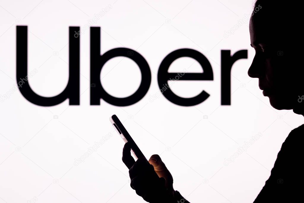 April 1, 2022, Brazil. In this photo illustration, a woman's silhouette holds a smartphone with the Uber Technologies logo in the background