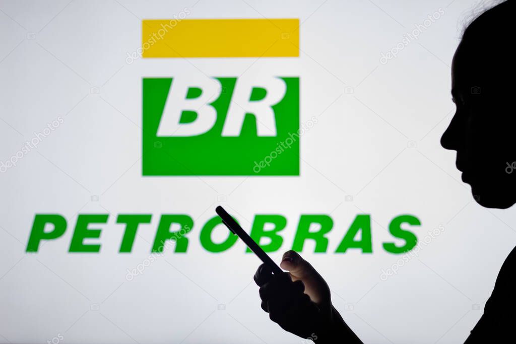 April 4, 2022, Brazil. In this photo illustration, a woman's silhouette holds a smartphone with the Petrleo Brasileiro S.A. (Petrobras) logo in the background.