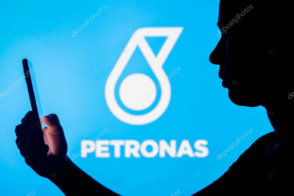 April 4, 2022, Brazil. In this photo illustration, a woman's silhouette holds a smartphone with the Petronas logo in the background