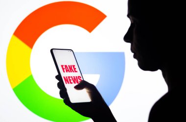 5 Nisan 2022, Brezilya. Bu resimde, bir kadın arka planda Google logosunun gösterildiği ekranda sahte haber logosu olan bir akıllı telefon tutuyor.