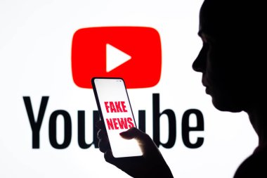 5 Nisan 2022, Brezilya. Bu resimde, bir kadın ekranda arkaplanda YouTube logosu sergilenen sahte haber logosuna sahip bir akıllı telefon tutuyor.