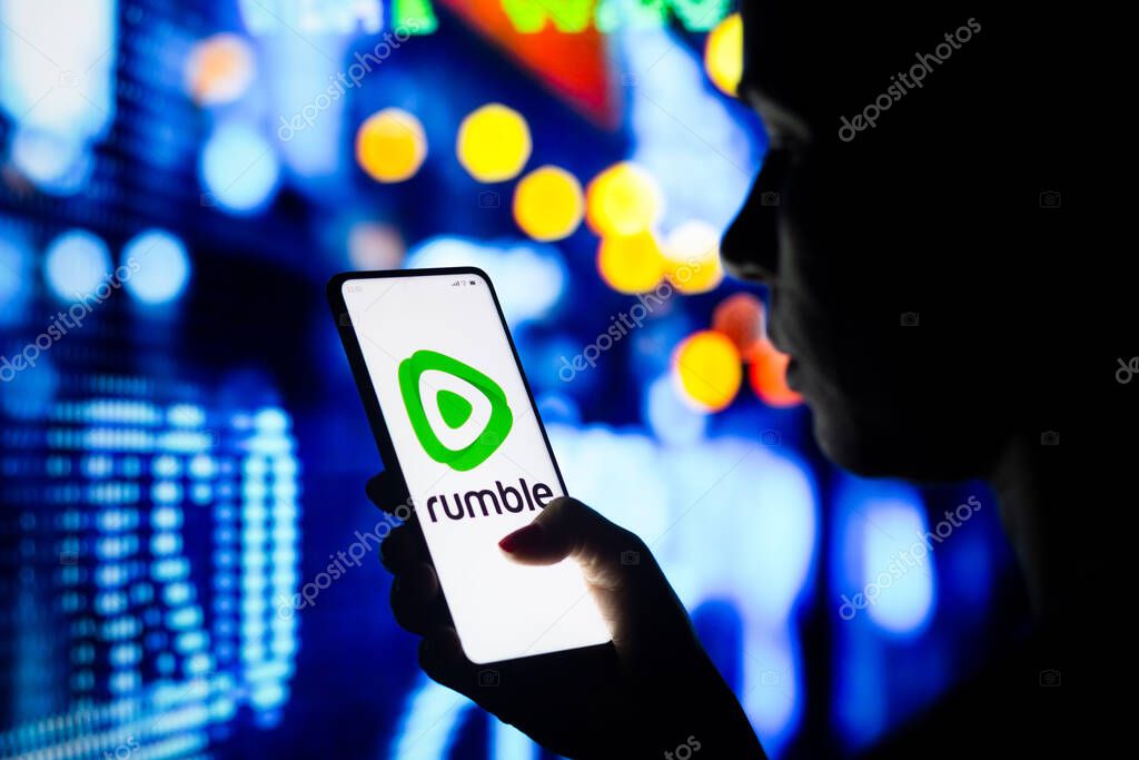 April 5, 2022, Brazil. In this photo illustration, a woman holds a smartphone with the Rumble logo displayed on the screen