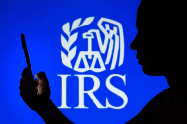 6 Nisan 2022, Brezilya. Bu resimde, bir kadının siluetinde arka planda Vergi Dairesi (IRS) logosu bulunan bir akıllı telefon bulunuyor.