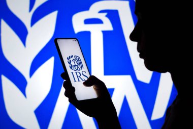 6 Nisan 2022, Brezilya. Bu resimde, bir kadının silueti ekranda ve arka planda Vergi Dairesi (IRS) logosunun gösterildiği bir akıllı telefon bulundurmaktadır.