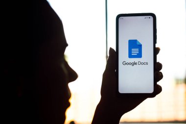 9 Nisan 2022, Brezilya. Bu resimde, bir kadının silueti ekranında Google Docs logosu olan bir akıllı telefon tutuyor.