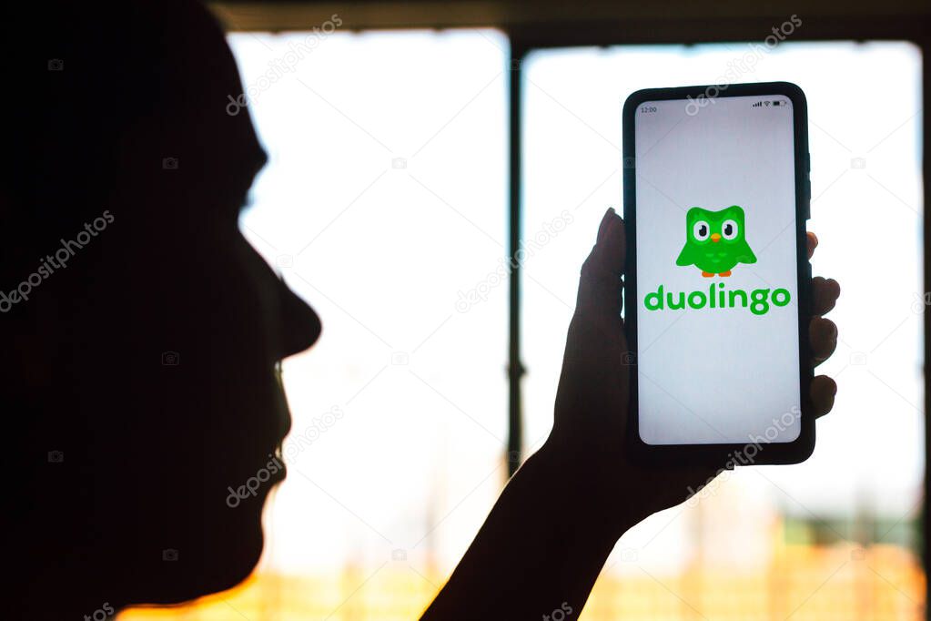 April 9, 2022, Brazil. In this photo illustration, a woman's silhouette holds a smartphone with the Duolingo logo displayed on the screen